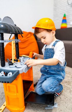 Tezgahta oynayan küçük bir çocuk. Kask takan bir çocuk oyuncaklarla dolu kapalı bir alanda oyuncak tezgahı olan bir binaya odaklanıyor..