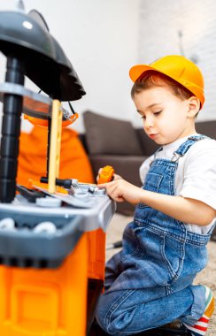 Çocuk aletlerle yaratıcı bir şekilde oynuyor. Genç bir çocuk, sert bir şapka takarken oyuncak alet takımıyla oynamaya odaklanır..