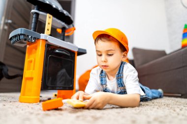 İçinde oyuncak mutfağı olan bir çocuk. Küçük bir çocuk oyuncak mutfak setiyle yaratıcı bir oyun oynuyor, bir inşaat şapkası takıyor ve etkinliğe odaklanıyor..