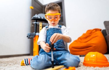 Çocuk yaratıcı bir şekilde inşa ediyor. Güvenlik gözlüklü küçük bir çocuk, içerideki halı döşemedeki araç ve gereçleri kullanarak bir proje yapıyor..