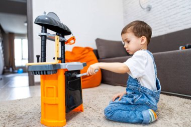 Çocuk içeride eğlencesine inşa ediliyor. Genç bir çocuk oyuncak tezgahıyla oynuyor, oturma odasındaki çeşitli bileşenleri oluşturmak ve etkileşim kurmak için aletler kullanıyor..