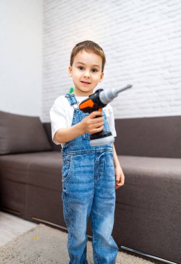 Oturma odasında elinde oyuncak matkabı olan çocuk. Genç bir çocuk oturma odasında elinde oyuncak matkapla duruyor, yaratıcı oyunlara ve projelere hazır..