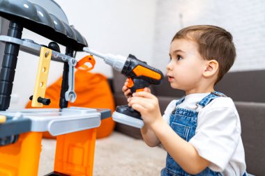 Evde oynayan çocuk müteahhit. Oyuncak tezgahıyla oynayan bir çocuk, evdeki etkinlikleri inşa etmek için oyuncak matkabını kullanıyor..