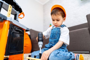 Çocuk aydınlık odada oyuncaklarla oynuyor. Küçük bir çocuk gündüz saatlerinde rahat ve renkli bir odada oyuncak aletlerle bir bina inşa etmeye odaklanır..