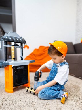 Çocuk oyuncak aletlerle oynuyor. Şapka takan genç bir çocuk oyuncak alet takımıyla oynuyor, parçaları birleştirirken merak ve odaklanma gösteriyor.