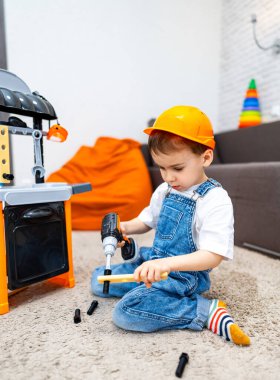 Çocuk yapı taşlarıyla oynuyor. Sabit şapka takan bir çocuk, oyun seti üzerinde oyuncak aletler kullanır. Etrafı renkli oyuncaklarla çevriliyken rahat bir odada..