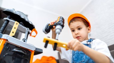 Çocuk oyuncak aletlerle oynuyor. Turuncu şapkalı bir çocuk oyun setinde oyuncak matkap ve aletler kullanır..