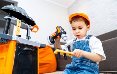 İçeride oyuncak aletler kullanan genç bir inşaatçı. Oyuncak alet takımıyla oynayan bir çocuk, kapalı bir alanda matkap ve ahşap bir parça kullanıyor..