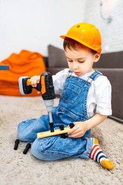 Çocuk oyuncaklarla inşa etmeyi seviyor. Oyuncak matkapla çalışan bir çocuk oyun sırasında tahta parçaları ve vidalar birleştirmeye odaklanmış..