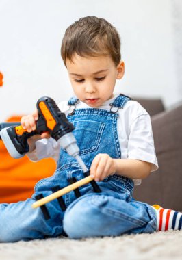 Aletlerle bir proje üzerinde çalışan bir çocuk. Genç bir çocuk ahşap bir projede çalışmak için matkapla yerde oturuyor. Parlak iç mekan ayarları odaklanmasını sağlar..