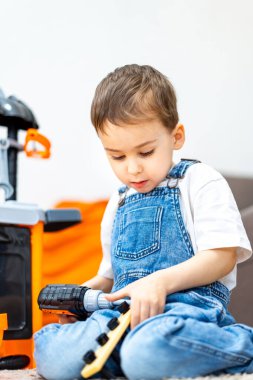 Çocuk oyuncak aletlerle oynuyor. Kot pantolon giyen genç bir çocuk ev ortamında renkli oyuncaklarla takılıyor..