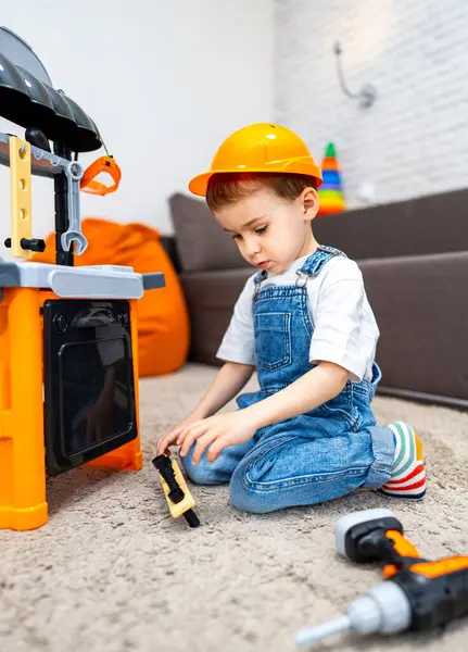 Çocuk içeride oyuncak aletlerle oynuyor. İnşaat şapkalı genç çocuk evde oyuncak aletlerle oynamaktan hoşlanıyor, oyundaki yaratıcılığı ve hayal gücünü vurguluyor.
