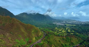 Göz kamaştırıcı yeşil arazide ilerliyoruz. Yeşil dağlarda otoyol. Gökyüzündeki bulutlu hava kayaların arasında. Vadideki Honolulu manzarası. Hawaii, ABD. Hava görünümü.