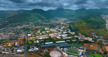 Düşük katlı şehir manzarası resim gibi yeşil dağlarla çevrili. Gökyüzünü kaplayan dramatik yağmurlu bulutlar. Honolulu, Hawaii, ABD. Hava görünümü.
