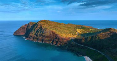 Güçlü kayalar Pasifik Okyanusu 'nun huzurlu mavi sularını kesiyor. Arabalar dağın sınırlarını çizen otoyolun yanından geçiyor. Hawaii, ABD. Hava görünümü.