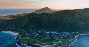 Büyük kayaların altında rahat bir yaşam alanı. Karayolu ile ana hatları çizilmiş sahilde bir yerleşim yeri. Oahu, Hawaii, ABD.