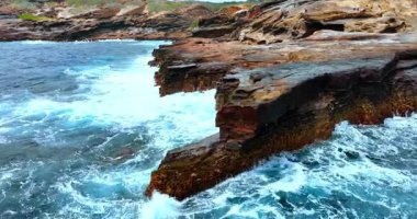 Kıyı şeridinin muhteşem engebeli kıyıları. Güçlü dalgalar kayalara çarpıyor. Bazı insanlar kayaların yanından geçer..