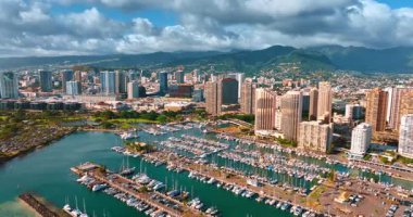 Rıhtımdaki çapanın üzerinde birden fazla yat duruyor. Pasifik Okyanusu 'nun yukarısından Honolulu, Hawaii, ABD kıyılarına yaklaşıyoruz. Gri bulutlar dağların üzerindeki gökyüzünde süzülür. Hava görünümü.