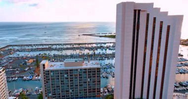 Harici asansörle otelin yüksek binası boyunca iniyorlar. Arka plandaki büyük yat kulübü. Hawaii, ABD.