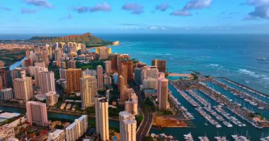 Pasifik Okyanusu 'nun su manzarası boyunca Waikiki binaları üzerinde uçuyorlar. Yat kulübünün birden fazla teknesi var. Diamond Head Krateri, arka planda batan güneşle aydınlandı. Hava perspektifi.