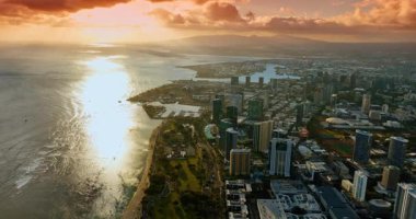 Honolulu, Hawaii, ABD sahilindeki yeşil parka yaklaşıyoruz. Batan güneş ışınları bulutların arasından geçer. Hava görünümü.