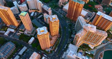 Yüksek binalar gün batımının turuncu ışığıyla aydınlatılıyor. Yolların üstündeki şehre hava perspektifi. Honolulu, Hawaii, ABD.