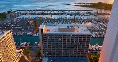 Pasifik Okyanusu sahilindeki çok katlı bir binaya yaklaşıyoruz. Arka planda büyük bir yat kulübü. Hawaii, ABD 'de günbatımı.