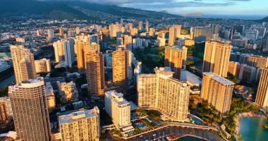 Yüksek binaların cephelerinde güneşin batışının parlak ışığı. Gün batımında Waikiki, Honolulu, Hawaii, ABD üzerindeki İHA uçuşu.
