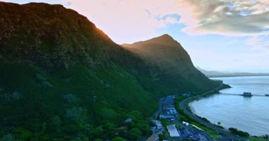 Dağın zirvesine yükseliyor ve arkasında saklanan güneşi açığa çıkarıyor. Parlak güneş manzarayı kamaştırıyor. Hawaii 'nin Rocky Sahili, ABD.