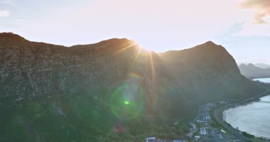 Dağın arkasında parlayan güneş manzarayı kamaştırır. İnsansız hava aracı görüntüsü, deniz manzarasının yakınındaki kayalıklarda bulunan yerleşim alanının üzerine iniyor..