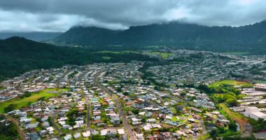 Düşük katlı villaları olan yoğun yerleşim alanları. Arkaplanda bulutlarla kaplı yeşil dağlar. Honolulu, Hawaii, ABD. Üst görünüm.