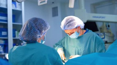 Profesyonel kadın cerrah metal aletlerle ameliyat yapıyor. Sıhhiyenin üstündeki lambalar açık..