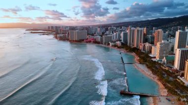 Pasifik Okyanusu dalgaları Waikiki, Honolulu, Hawaii, ABD 'nin kumlu sahillerine doğru akar. Gün batımında şehrin havadan görüntüsü. Arkaplanda bulutlu gökyüzü.