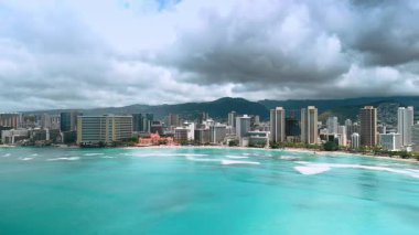 Turkuaz su manzarasının üzerinden uçarak Waikiki ufuk çizgisine yaklaşıyoruz. Şehir manzarasının üzerinde asılı dramatik yağmurlu bulutlar. Hava görünümü.