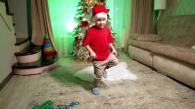 Noel Baba şapkalı enerjik çocuk odada zıplıyor ve kıvrılıyor. Çocuk Noel 'de evde eğleniyor..