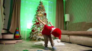 Kırmızı tişörtlü çocuk Noel Baba şapkasını yüzüne doğru çekti. Noel için evde enerjik bebek oyuncakları.