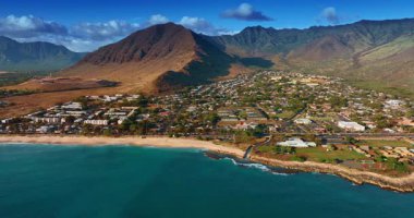 Güneşli bir günde Hawaii kıyısı boyunca uçmak. Mavi suların üzerinde insansız hava aracı görüntüleri. Arkaplanda engebeli dağlar. Hava görünümü.