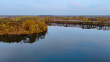 Hollanda manzarasının havadan görünüşü. Hollanda 'da alacakaranlıkta yemyeşil ve sarı ağaçlarla çevrili sakin bir göl manzarası..