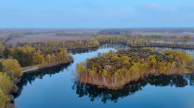 Hollanda 'da, sudaki yeşil ada. Hava manzarası, sakin bir su kütlesi içinde sakin yeşil bir ada ve alacakaranlıkta uzak tarlalar gösteriyor..