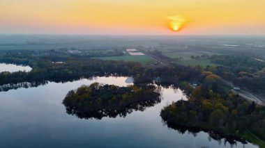 Göllü Hollanda manzarasının üzerinde gün batımı. Hollanda 'da yemyeşil ve tarlalarla çevrili sakin bir göl üzerinde hava manzarası güzel bir gün batımı yakalar..