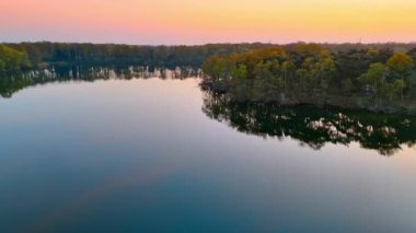 Gün batımında Hollanda 'nın doğal güzelliği. Hava manzarası ağaçlarla çevrili sakin gölü yakalar, suyun yüzeyindeki yumuşak günbatımı renklerini yansıtır..