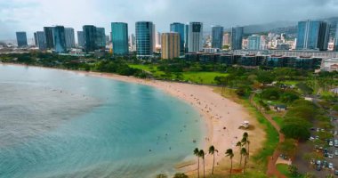Yeşil park ile çevrili güzel kumlu sahil. Waikiki 'nin modern yüksek binaları arka planda. Hawaii, ABD.