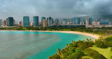 Waikiki, Honolulu, Hawaii, ABD 'deki kumlu sahilde turkuaz su. Modern şehrin modern siluetine yaklaşıyoruz. Arkaplanı kaplayan kalın bulutlu manzara.