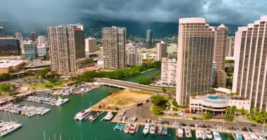 Waikiki kıyısındaki çapanın üzerinde modern yatların üzerinde uçuyor. Rıhtımdaki yüksek binalara yaklaşıyoruz. Arkaplanı kaplayan koyu bulutlu manzara.