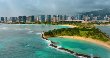 Taştan barajın kenarından gelen dalgalar çarpıcı doğayla güzel kumlu sahili koruyor. Waikiki ufuk çizgisinde bulutlu bir zemin ile hava görüntüsü.