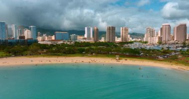 Tatilciler kumlu sahilde dinlenir ve turkuaz suda dururlar. Waikiki, Honolulu, ABD 'nin tatil beldesi. Rıhtım boyunca uçuş. Arkaplanda dramatik bulutlu manzara.