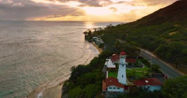 Dağ eteğindeki pitoresk sahilde beyaz deniz feneri. Gün batımında Pasifik Okyanusu 'nun havadan görünüşü.