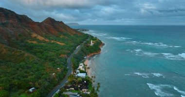 Volkanik dağların pitoresk yamaçları boyunca uzanan otoyol. Kalın bulutlar ufuktaki gökyüzünü kaplıyor. Hawaii, ABD. Hava görünümü.