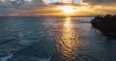 Batan güneş bulutların arkasından görünüyor. Güzel okyanus Honolulu, Hawaii, ABD sahillerine dalgalar gönderiyor. Hava görünümü.