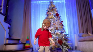 Havacı şapkalı gülümseyen bebek Noel ağacının yanında oturuyor. Çocuk güneş gözlüğü takmak istiyor ama fikrini değiştirip gidiyor..